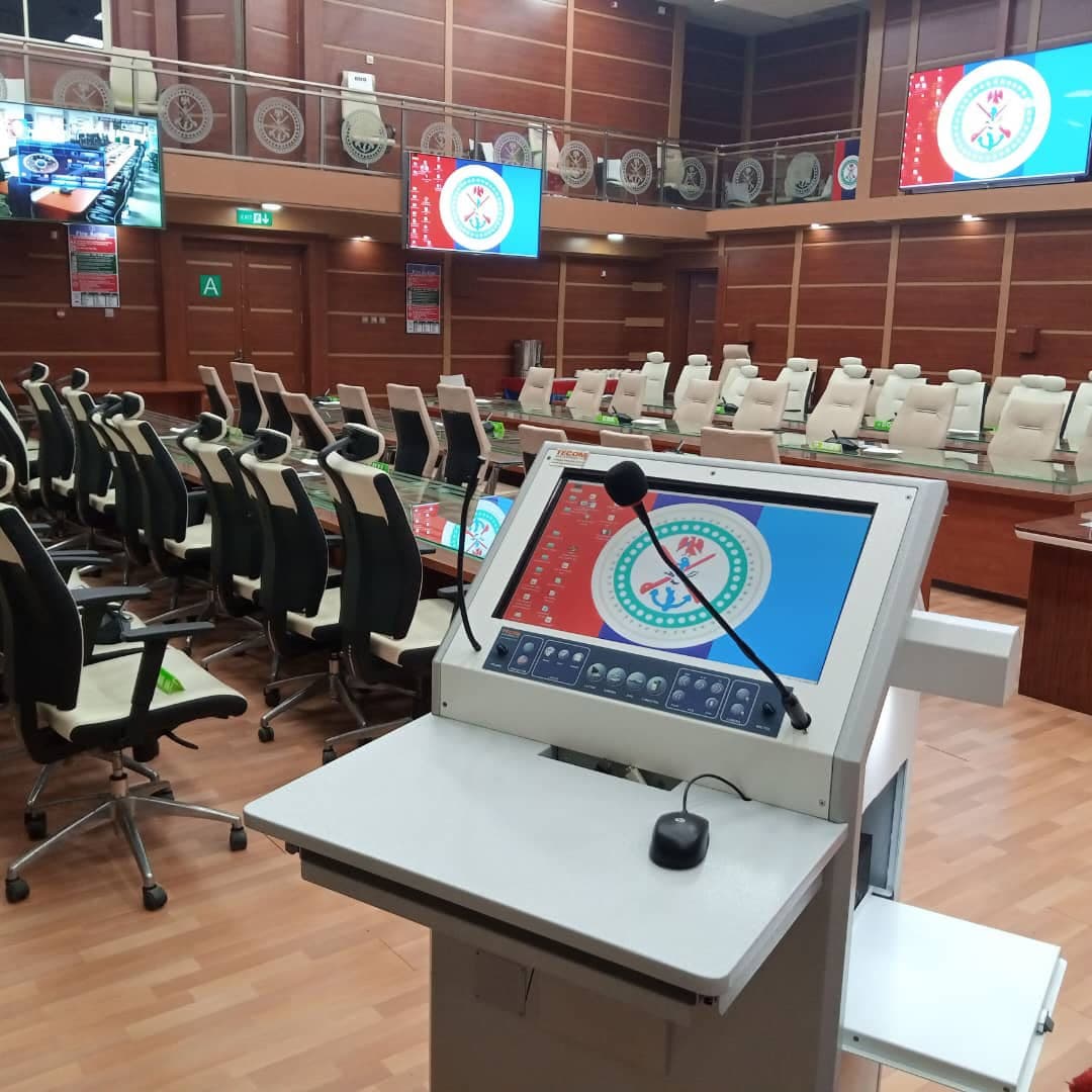 Conference room with a multimedia lectern in the foreground, delegate microphones along curved tables and wall-mounted displays